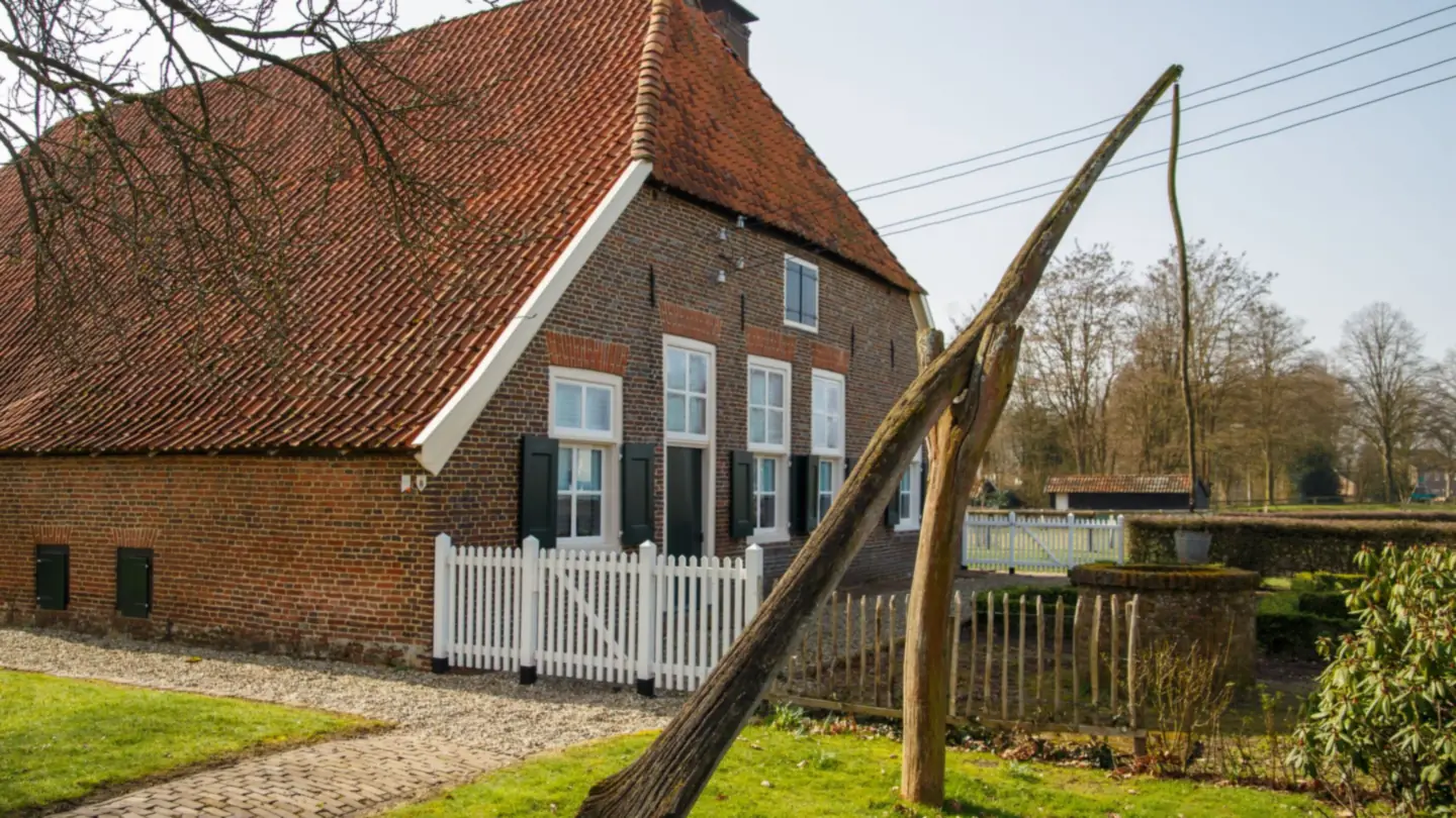 Bakstenen boerderij met rood pannendak, luiken en een wit hekje
